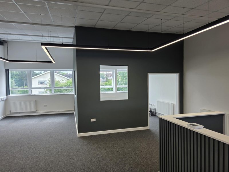 Finished open-plan office with black linear pendant lighting, a dark feature wall and a slatted reception counter