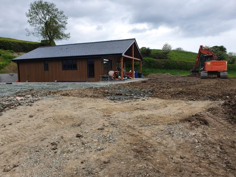 Completed timber-clad lodge with groundwork still open in front of it