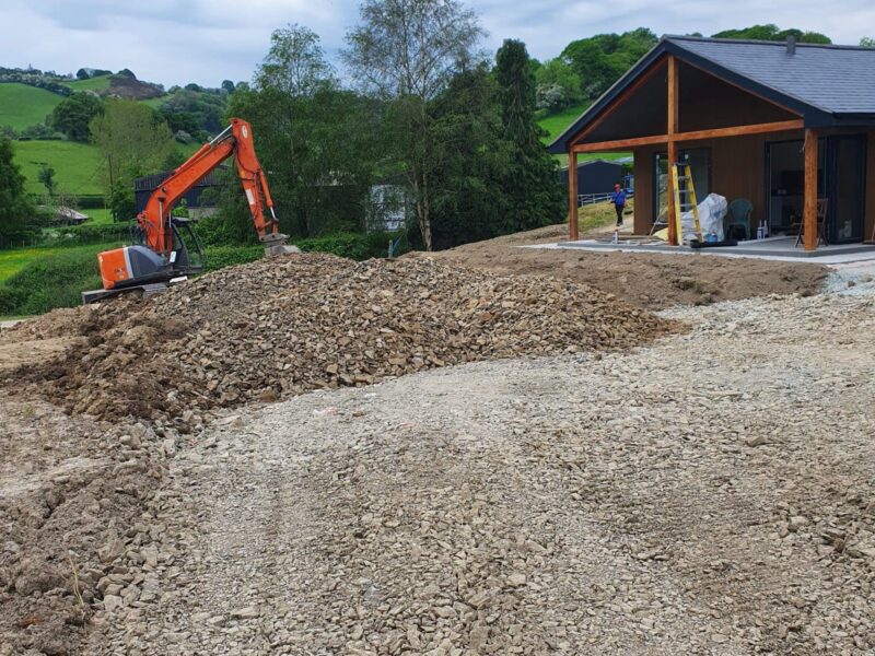 Excavator working on the lodge site with a stone access track laid across bare ground