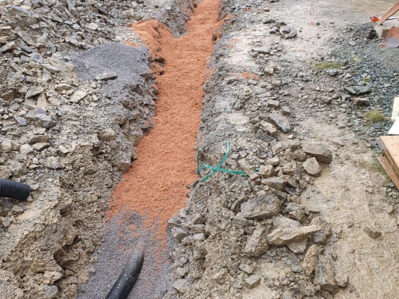 Drainage trench cut through stone with ducting laid ready for backfilling