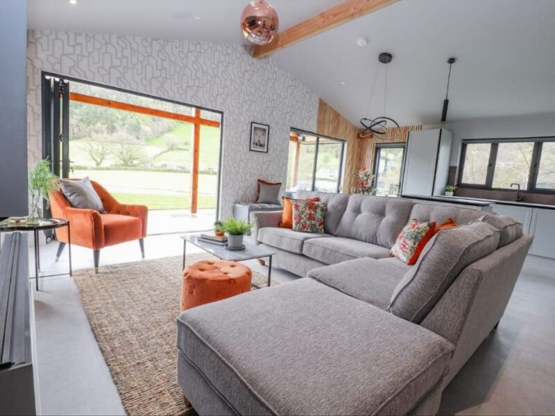 Lounge with a corner sofa and an armchair, opening onto the valley through full-height glazed doors