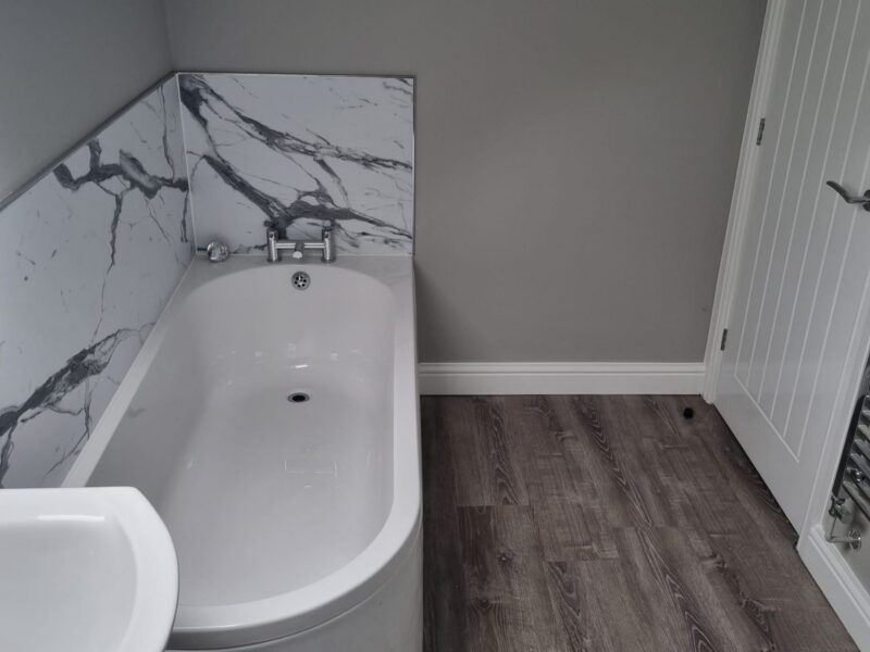 Bathroom with a corner bath, marble-effect panelling and a basin