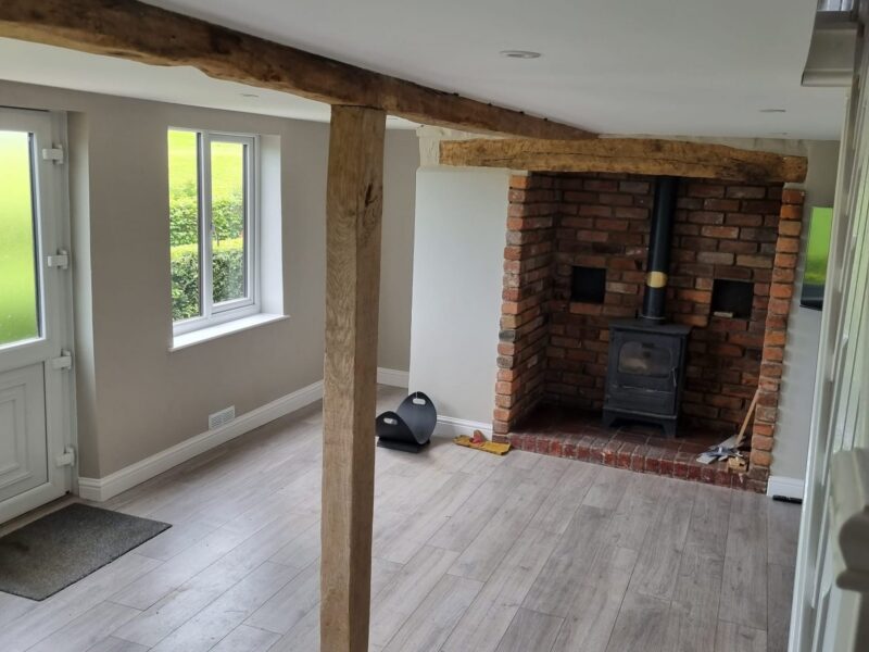 Lounge with a wood burning stove in an exposed brick fireplace beside an oak post