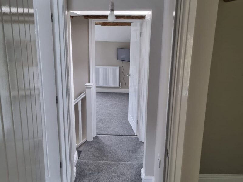Hallway with a panelled door, looking through to a carpeted room beyond
