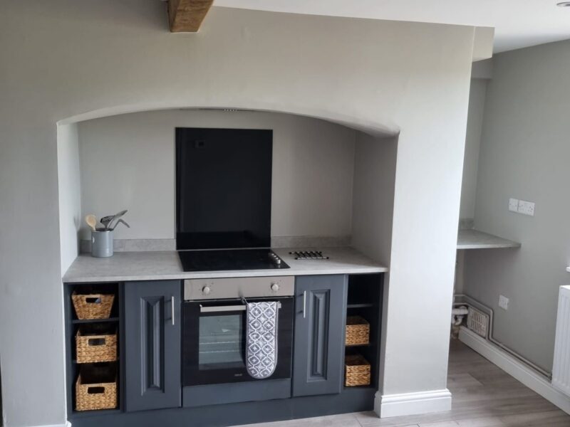 Kitchen with dark units set into an arched recess beneath an exposed beam
