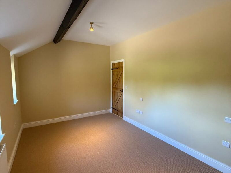 Bedroom with a dark beam across the sloped ceiling, a ledge-and-brace timber door and fitted carpet