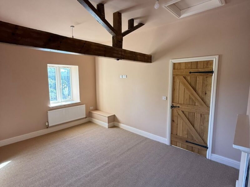 Bedroom beneath exposed roof trusses, with a ledge-and-brace timber door, a loft hatch and fitted carpet