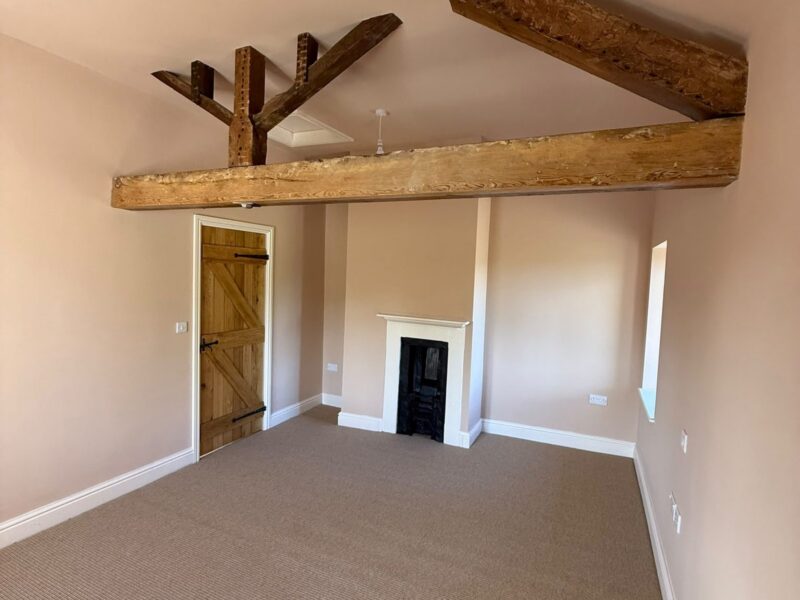 Bedroom beneath an exposed truss, with a ledge-and-brace timber door, a small cast-iron fireplace in a painted surround and fitted carpet