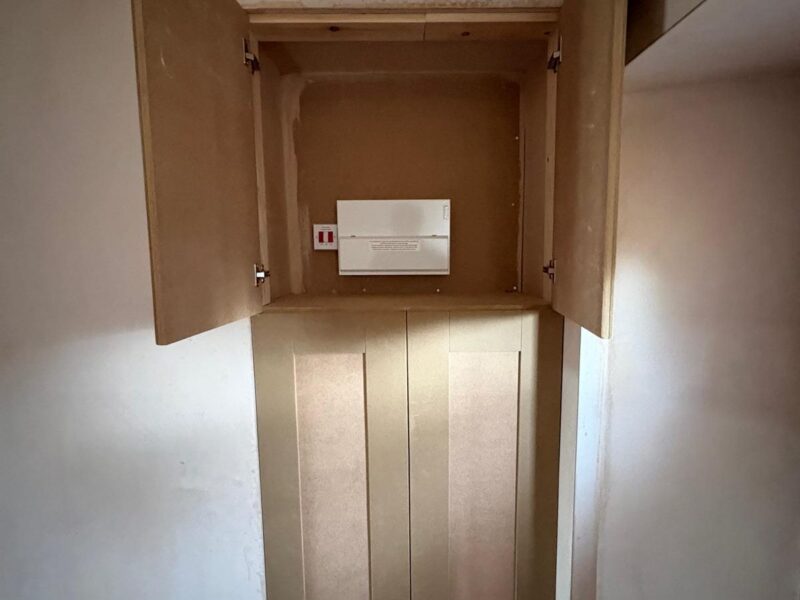 Consumer unit housed in a new fitted cupboard, its doors open against a plastered wall