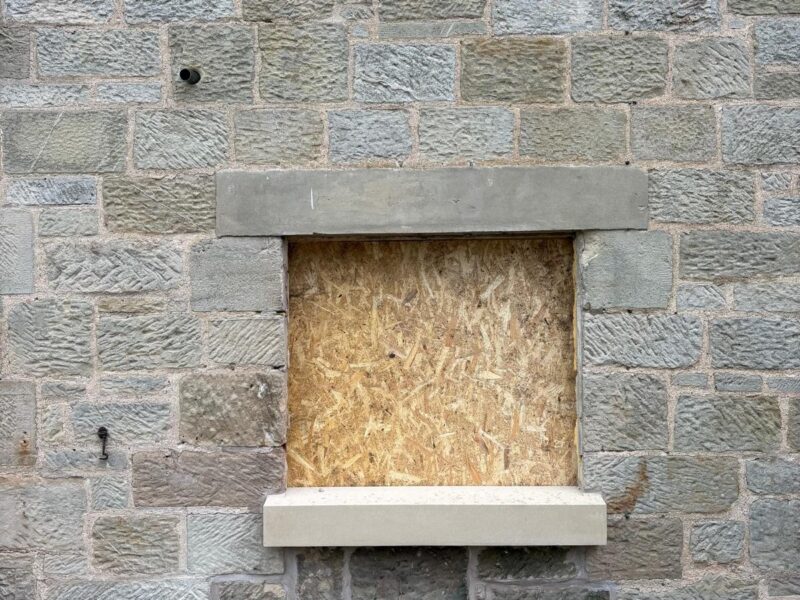 New stone lintel and cill set into the stone elevation, with the opening boarded over