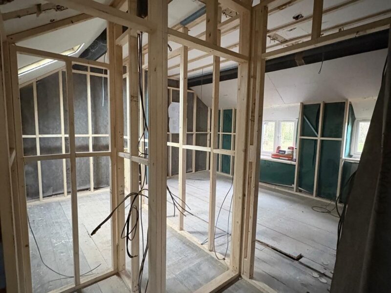 New stud partitions framed off the existing floorboards, with cabling run through them and a roof window in the slope beyond
