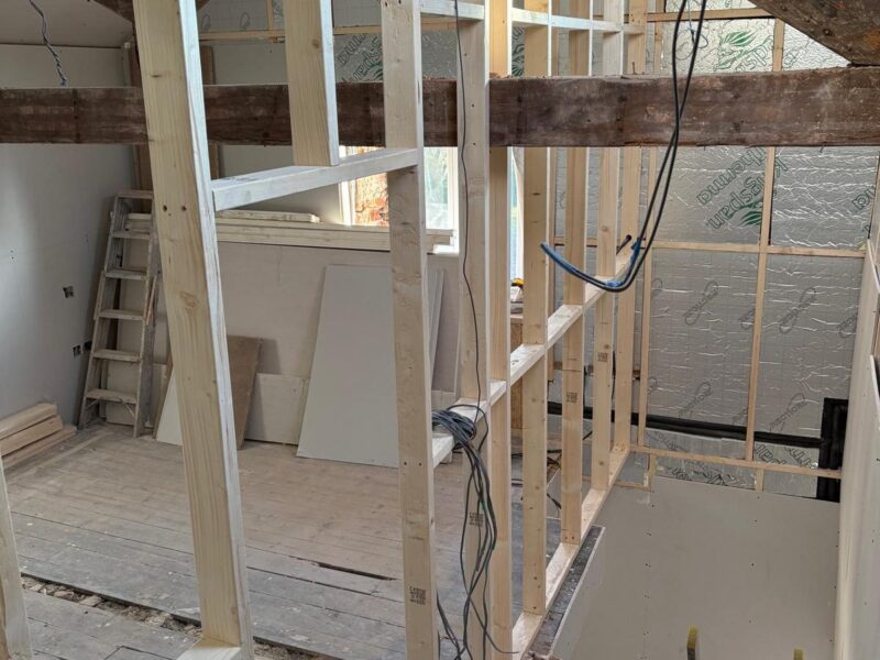 Stud partitions framed up to the rafters, with foil-faced insulation board fitted between the studs and plasterboard sheets stacked ready