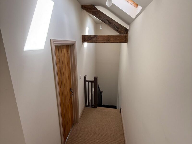 Landing with a roof window, an exposed beam, an oak plank door and the stair balustrade beyond