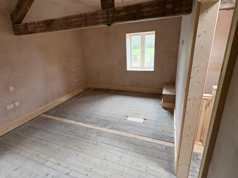 Bedroom plastered out beneath exposed roof trusses, with a new door lining fitted and the floorboards bare