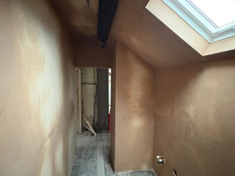 Landing plastered out beneath a roof window, with a dark beam crossing the ceiling and the floorboards bare