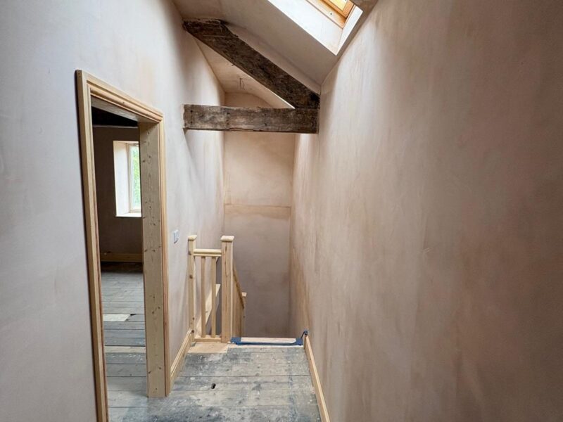 Landing plastered out beneath a roof window, with the new staircase balustrade framed up at the far end