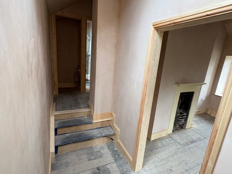 Stairs and landing plastered out, with new architrave around an opening into a room with a fireplace