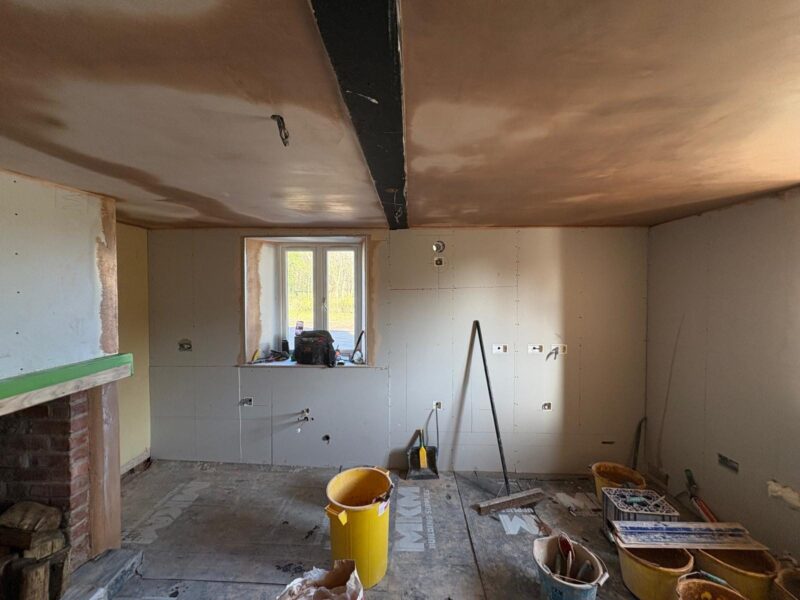 Plasterboarding underway around a brick fireplace opening, with mixing buckets and tools across the floor