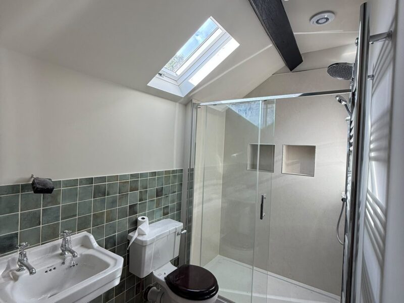 Shower room with a sliding-door enclosure, a traditional basin, a WC and green tiling, lit by a roof window beneath a dark beam