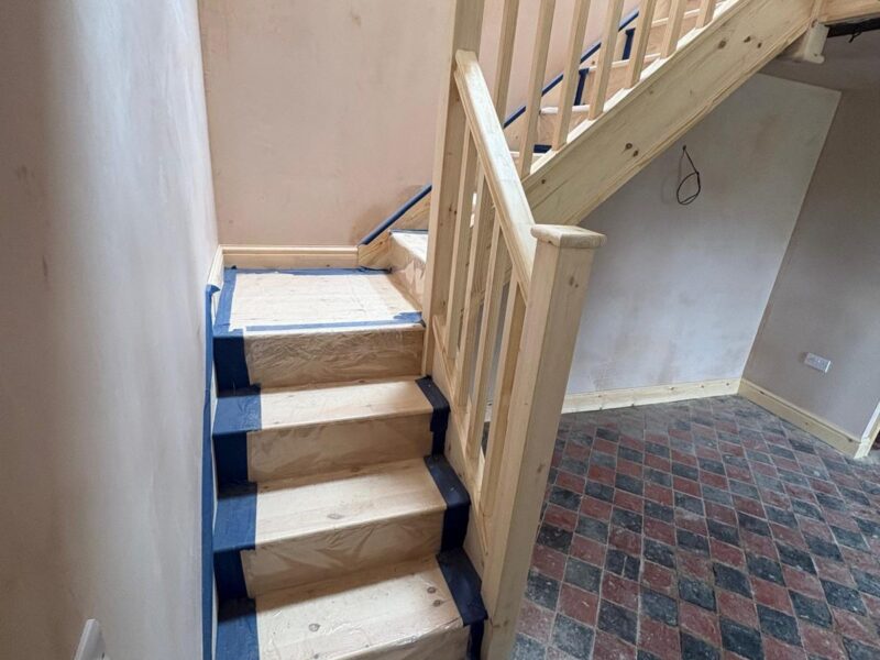 New staircase fitted, its treads boarded and taped for protection, with a bare timber balustrade above a tiled floor