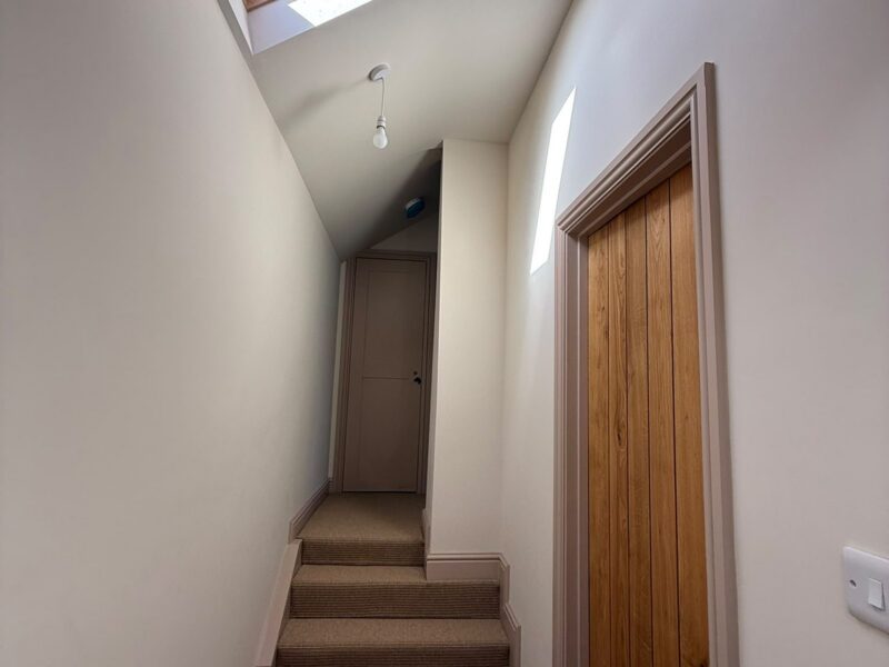 Stairs rising to a painted door, lit by a roof window, with an oak plank door alongside