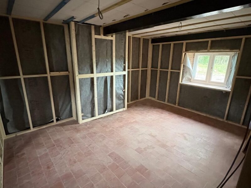 Stud walls framed against a dark membrane lining, with a new window fitted above a brick-paved floor